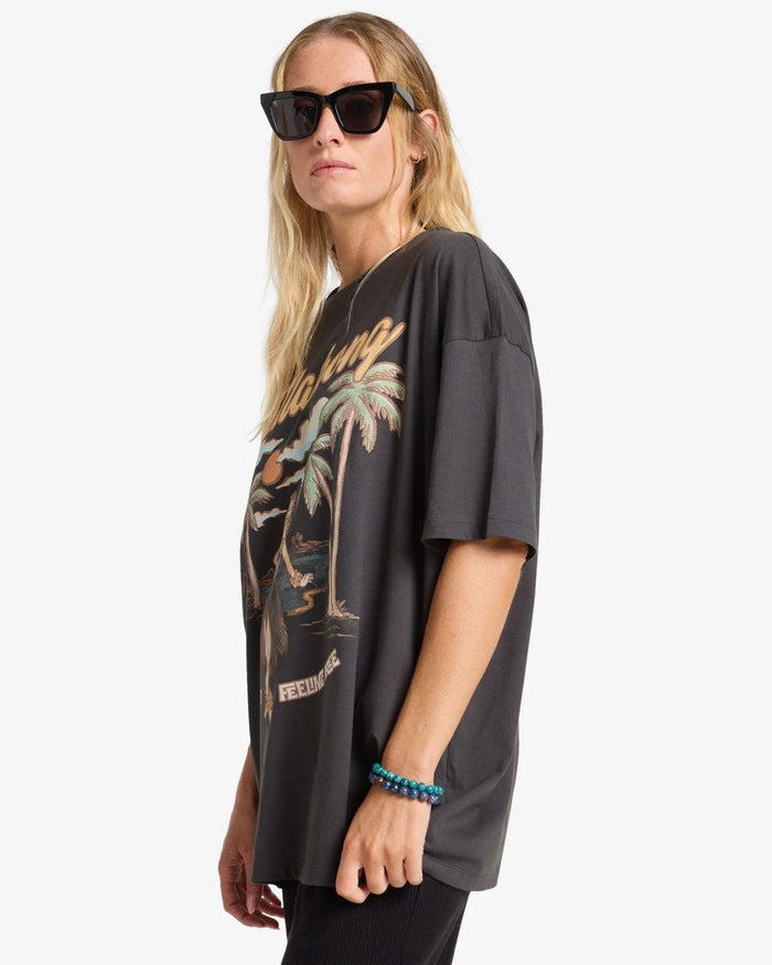 Woman wearing a billabong black oversized t-shirt with palm tree design on a white background