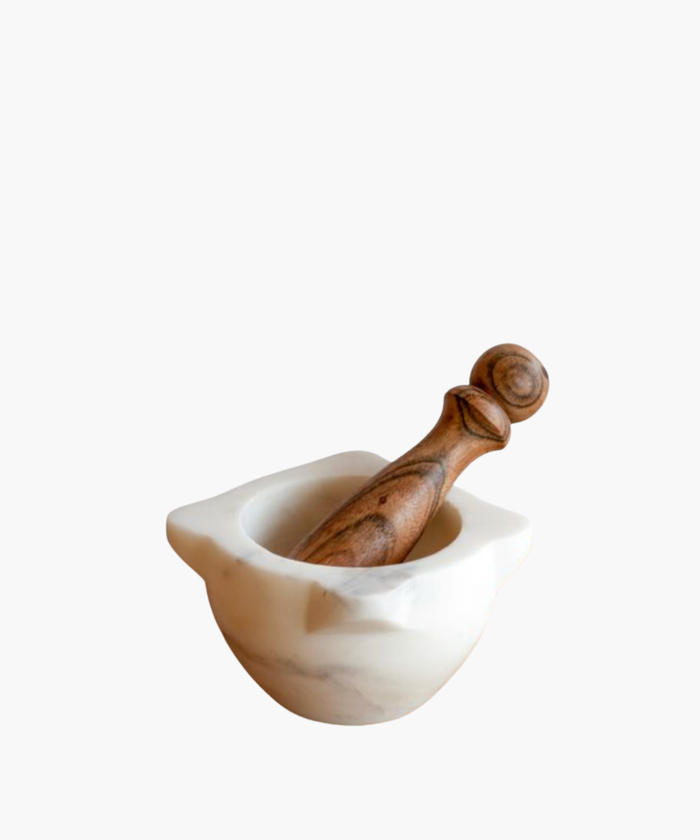 A marble mortar with a wooden pestle resting inside. The mortar is smooth and white, contrasting with the textured, brown wood of the pestle. | Wildwood Home Co.