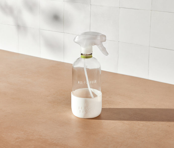 A refillable Glass All-Purpose bottle, used to dilute and dispense Branch Basics Concentrate with water, displayed on a neutral surface and white tiled background.