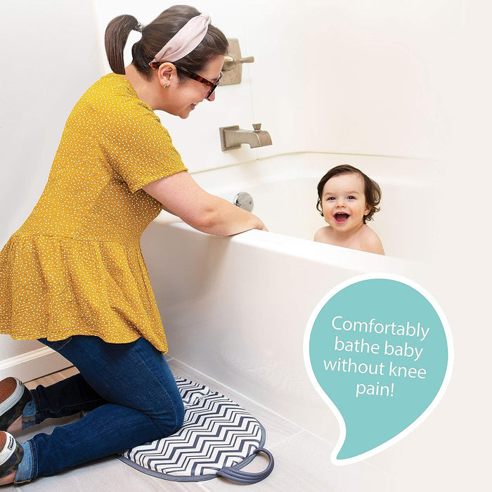 A woman kneels on a cushioned mat with a bathtub arm rest from the Baby Bathtime Essentials Bundle, smiling at her baby in the tub. A speech bubble says, Comfortably bathe baby without knee pain!.