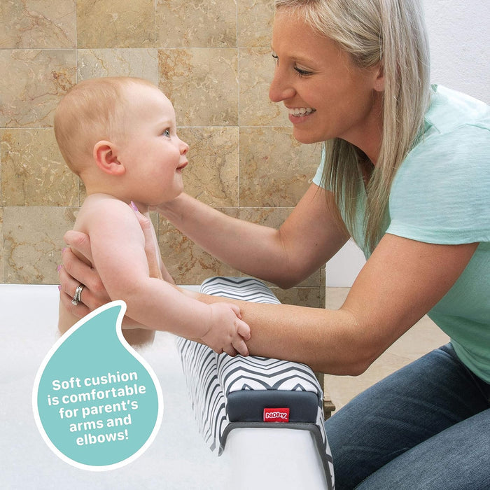 A smiling woman uses the Baby Bathtime Essentials Bundle, kneeling by a tub and holding a baby. A cushioned arm rest supports her arms for comfort. Text bubble: "Soft cushion is comfortable for parents’ arms and elbows!.