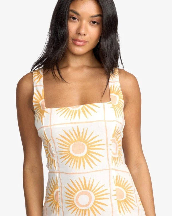 Woman wearing a billabong white mini dress with yellow sun patterns on a plain background