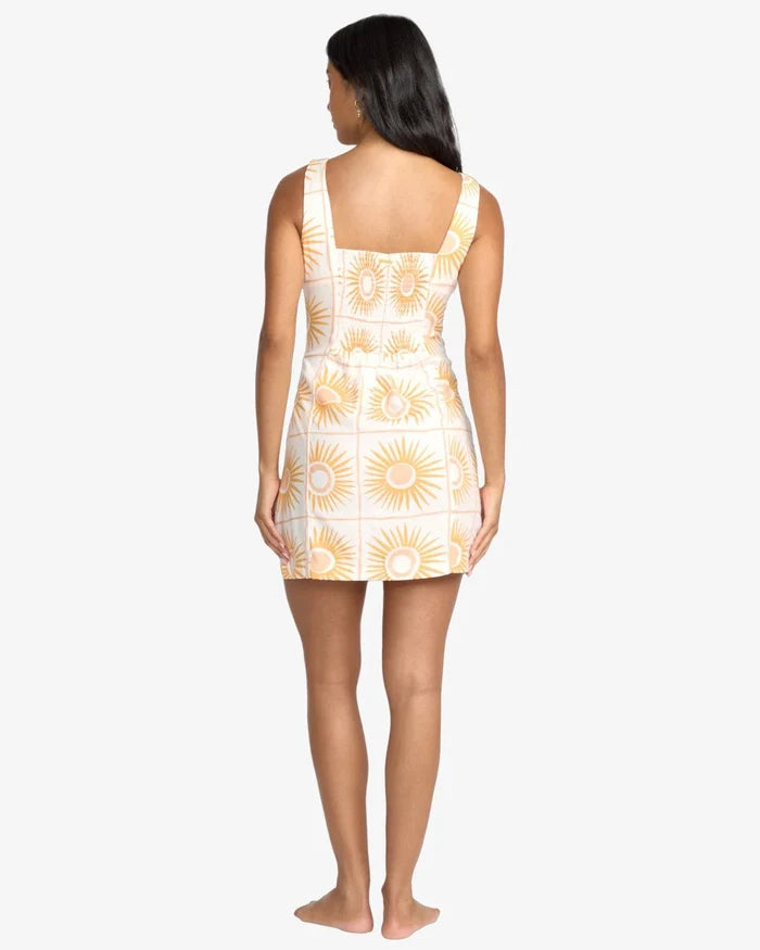 Woman wearing a white billabong dress with yellow floral patterns on a white background