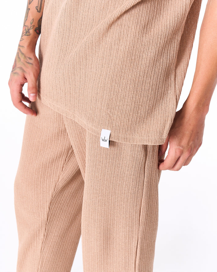 Martin Valen Breeze Fit men's tracksuit in beige, close-up front view of ribbed knit fabric and visible brand tag with tattooed hand at side.
