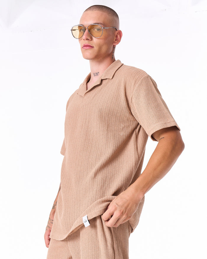 Martin Valen Breeze Fit men's tracksuit in beige, low-angle bust shot showing ribbed polo top and yellow-tinted sunglasses.