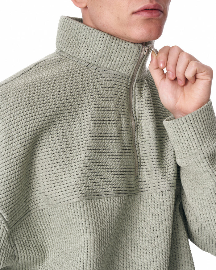 Martin Valen khaki high‑collar half‑zip tracksuit, mid shot of model with crossed arms wearing aviator sunglasses