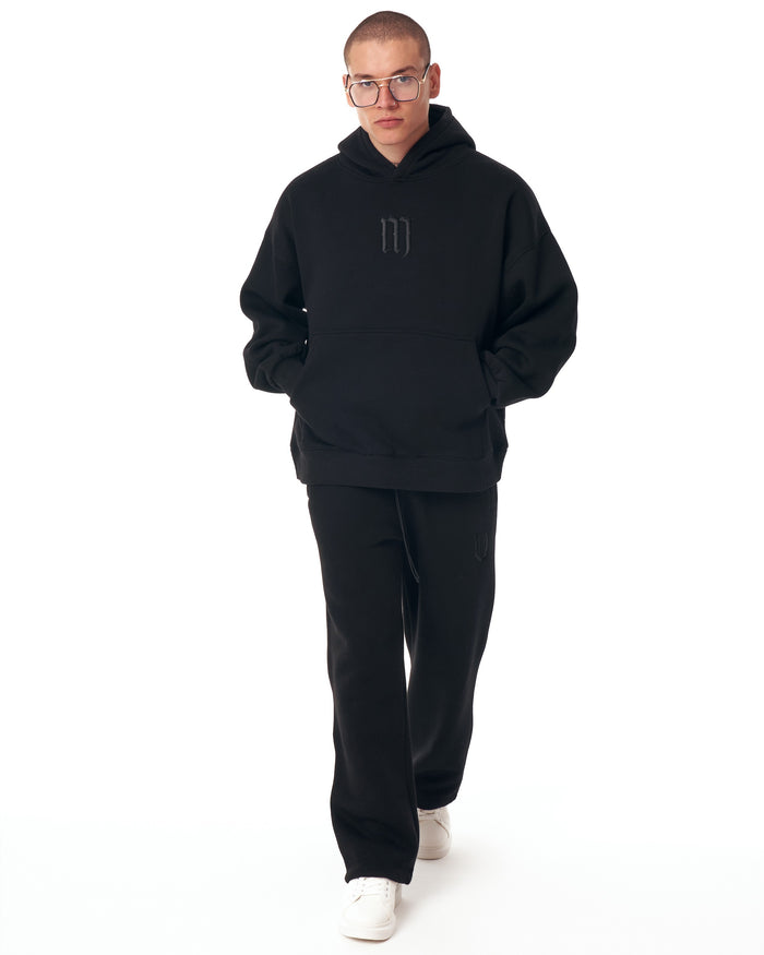 Martin Valen Insignio oversized black hoodie tracksuit front view, 3D embroidered logo on chest and kangaroo pocket, model standing