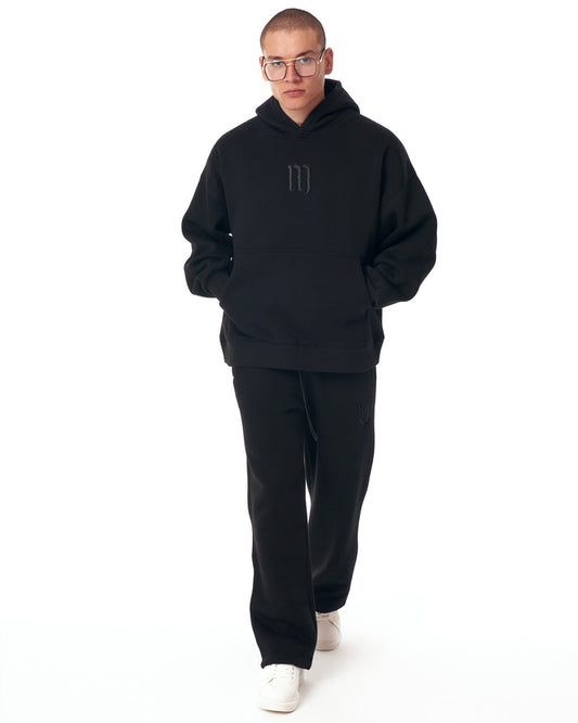 Martin Valen Insignio oversized black hoodie tracksuit front view, 3D embroidered logo on chest and kangaroo pocket, model standing