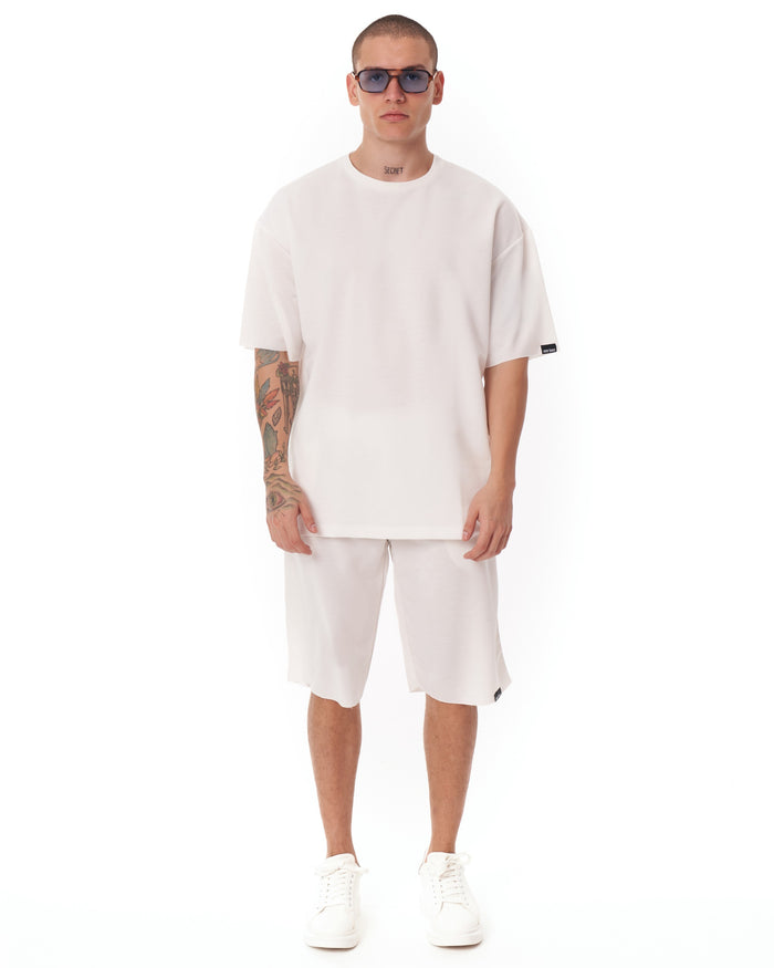 Martin Valen men's oversized white shortsuit, front view showing light fabric and black logo tag on sleeve.