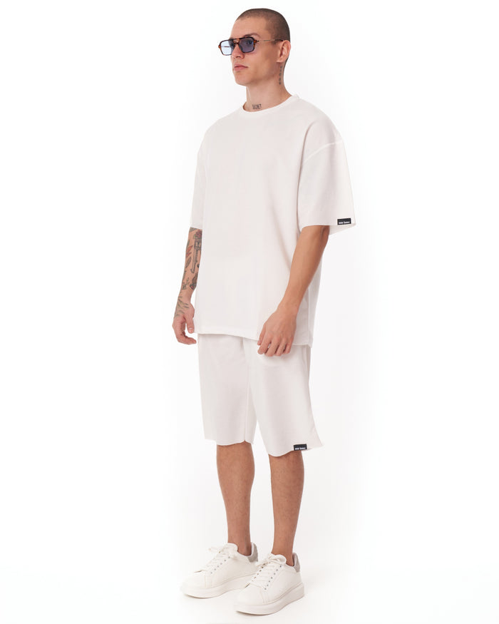 Martin Valen men's oversized white shortsuit, three-quarter view highlighting knee-length shorts and white sneakers.