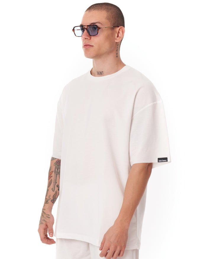 Martin Valen men's oversized white shortsuit, side view showing roomy cut and black logo tab at the shorts' hem.