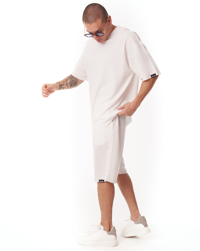 Martin Valen men's oversized white shortsuit, side mid-body and leg view, shorts with hem label and white sneakers with grey heel tab