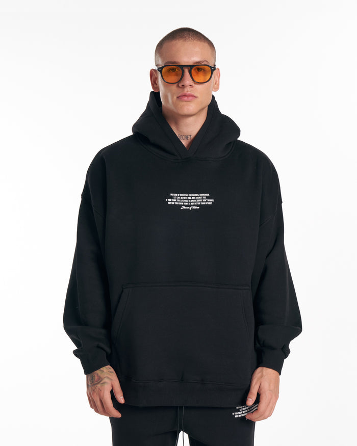 Martin Valen Rumi oversized black hoodie and track pants, walking front view showing right leg print and sneakers