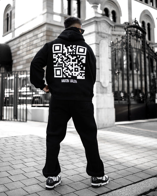 Martin Valen Sigilio oversized black hoodie seen from rear, large white QR code printed on the back, three-quarter view.
