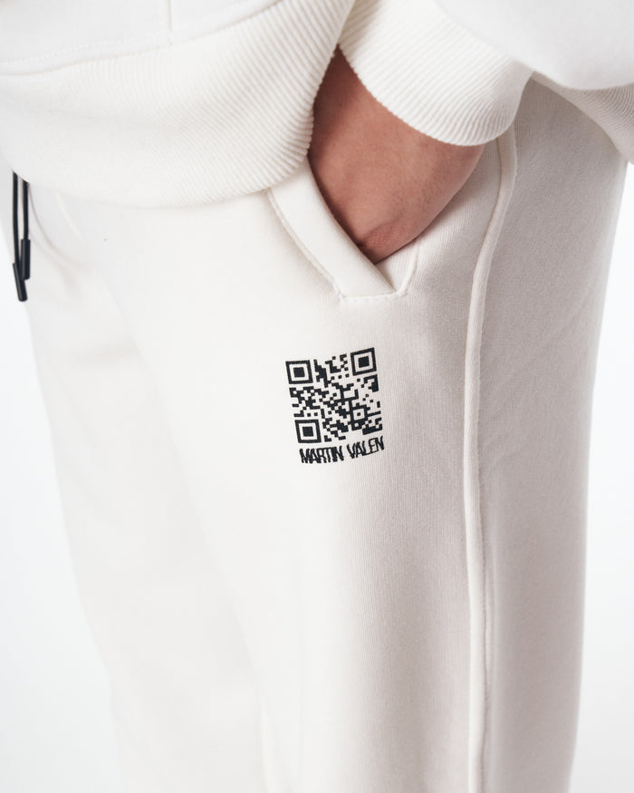 Martin Valen Sigilio white hoodie tracksuit mid-shot, model looking down with hood up and QR code visible on thigh