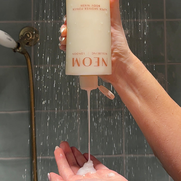 NEOM super shower power body wash upside down being squeezed into a persons hands in the shower