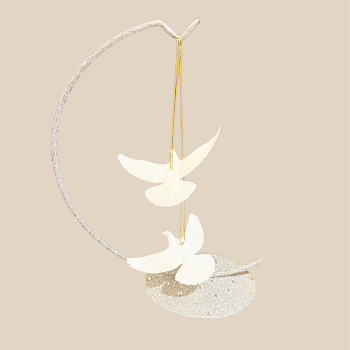 two white turtle dove hanging ornaments featuring two doves suspended from a curved silver branch-like frame on a plain beige background.